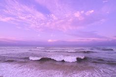 the sky is pink and purple over the water at the ocean shore with waves coming in to shore