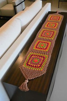 a crocheted table runner with tassels on it sitting on top of a white couch