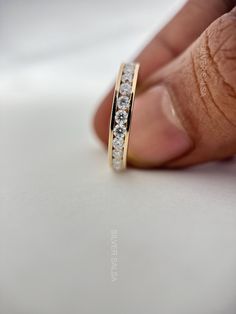 a hand holding a gold ring with white stones on it's side and the middle finger