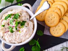 a white bowl filled with dip next to crackers and parsley on a table