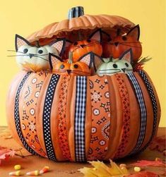 two cats sitting in a pumpkin shaped basket on top of a wooden table with autumn leaves