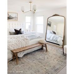 a bedroom with a large white bed and mirror on the wall next to a bench