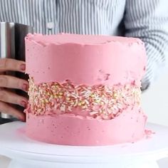 a pink cake with sprinkles on it being held by a woman's hands