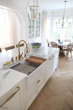 a white kitchen with marble counter tops and gold faucets on the sink area