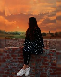 a woman sitting on top of a brick wall next to a red and orange sky