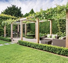 an outdoor living area with green grass and wooden pergoline, surrounded by greenery