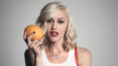 a woman holding an orange in her right hand and looking at the camera while wearing a white tank top