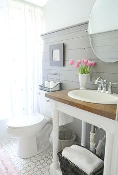 a white toilet sitting next to a sink in a bathroom under a mirror and a wooden counter top