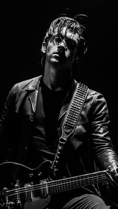 a man with a guitar in his hand and wearing a leather jacket, sitting on a chair