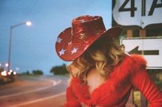 a woman wearing a red cowboy hat standing on the side of a road at night