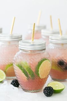 four mason jars filled with lemonade and blackberries, limes and strawberries