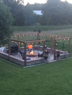 a backyard with a fire pit surrounded by lawn furniture and string lights on the patio