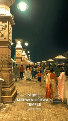 there are many people walking down the street at night time in this photo, one is wearing an orange and white sari