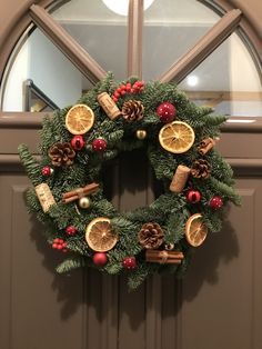 a christmas wreath with oranges, pine cones and other decorations hangs on the front door