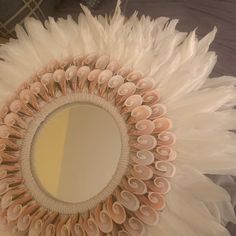 a mirror with white feathers on it sitting on top of a bed next to a wall