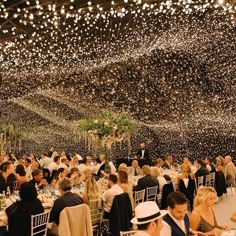 a large group of people sitting at tables in a room with lights on the ceiling