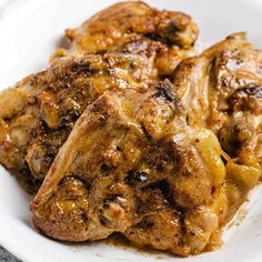 three pieces of chicken on a white plate with brown gravy over it and another piece of meat in the background