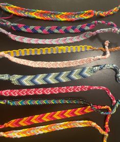 four different colored braided bracelets are lined up on a black surface and one is empty