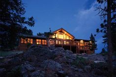 a house lit up at night on top of a hill with rocks and trees around it