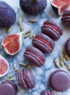 purple macaroons and figs are arranged on a marble counter top with nuts