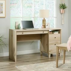 a wooden desk with a laptop on top of it next to a chair and potted plant