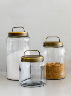 three glass jars with gold lids are sitting on a white countertop next to each other