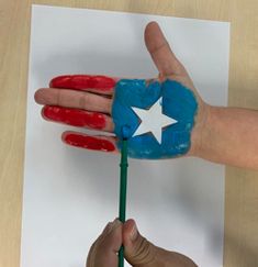 a hand with a star painted on it is holding a green stick in front of a piece of paper