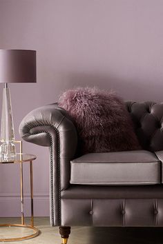 a grey leather couch with purple pillows and a lamp on the side table next to it