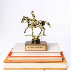 a gold statue of a man riding a horse on top of three stacks of books