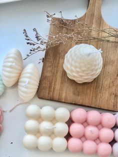 some pink and white beads are on a wooden cutting board next to other colored beads