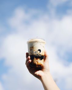 a person holding up a cup with ice cream on it in front of a cloudy blue sky