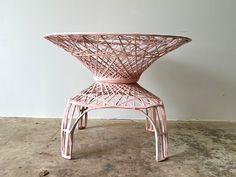 a pink wicker chair sitting on top of a cement floor next to a white wall