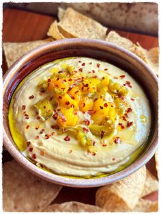 a bowl filled with hummus and crackers on top of a wooden table next to tortilla chips