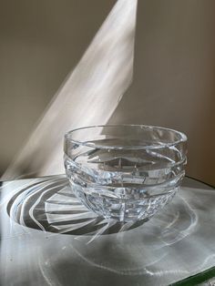 a clear glass bowl sitting on top of a table next to a shadow cast object