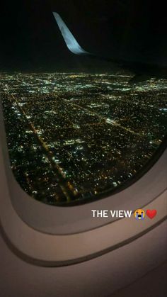 an airplane window with the view of city lights at night from it's wing