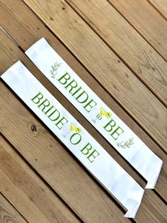 two bride to be sashes sitting on top of a wooden floor