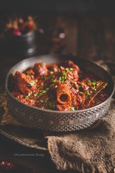 a metal bowl filled with meat and vegetables on top of a table next to a cloth