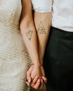 two people holding hands with tattoos on their arms and one has a mountain tattoo on his arm