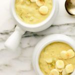 two white bowls filled with soup on top of a marble counter next to silver spoons