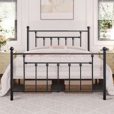 a white bed with black metal frame and headboard in a bedroom area next to two windows