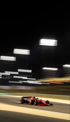 a red race car driving down a track at night