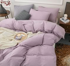 an unmade bed with purple sheets and pillows on the floor next to a table