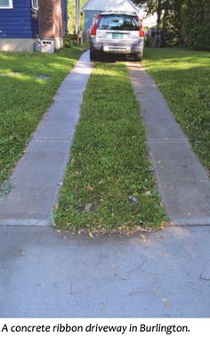 a car parked in front of a house on a sidewalk with grass growing between the curb