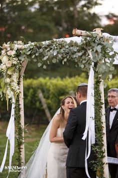 the bride and groom are smiling at each other as they stand under an arch with greenery