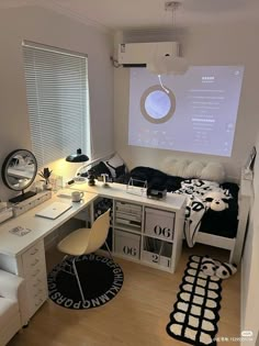 a room with a bed, desk and computer monitor on the wall next to it