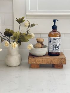 a bottle of hand soap sitting on top of a wooden stand next to a vase with flowers