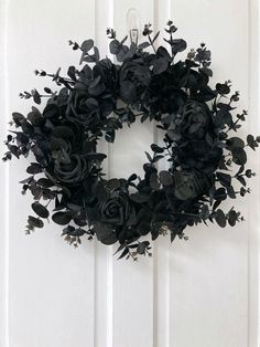 a black wreath is hanging on a white door with flowers and leaves around it,