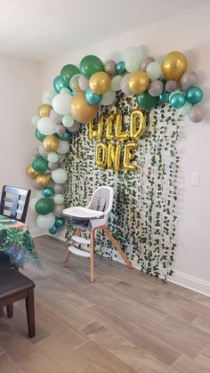 a party room with balloons and streamers on the wall that says wild one in gold