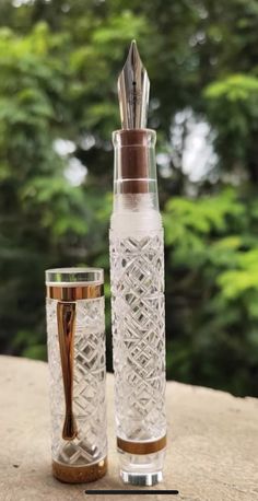 two glass vases sitting next to each other on top of a stone slab with trees in the background