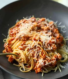 spaghetti with meat sauce and parmesan cheese in a black bowl